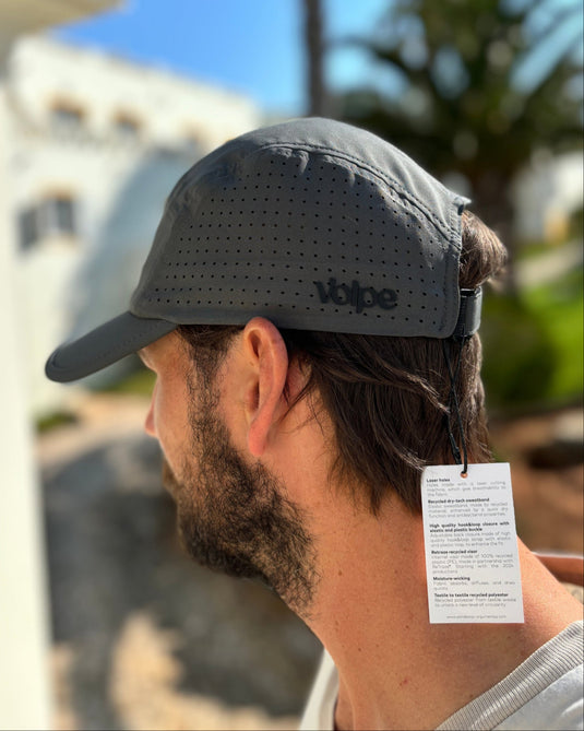 Man wearing a gray cap with branding, standing outdoors.