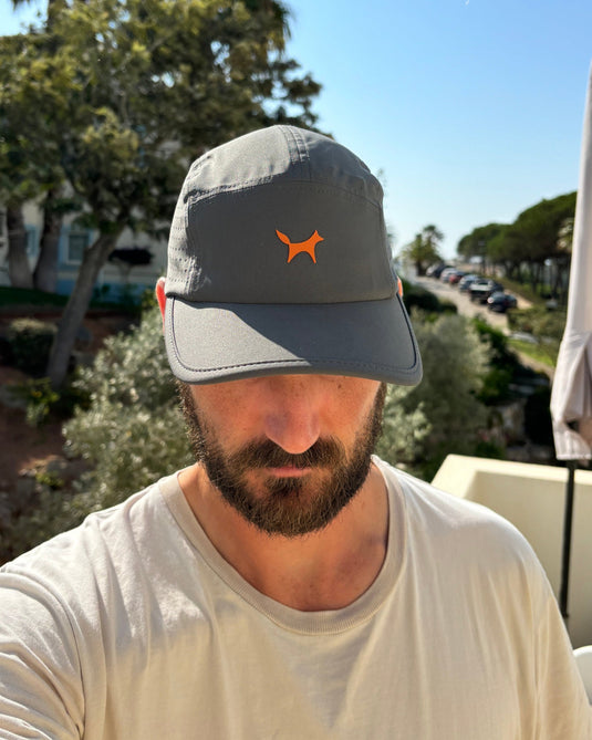 Man wearing a gray cap with an orange logo outdoors