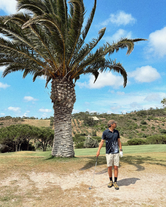 Lifestyle photo of golfer with charcoal Volpe polo in front of a date palm tree